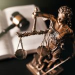 Bronze statue of Lady Justice holding scales with a gavel and book in the background, representing legal principles in insurance
