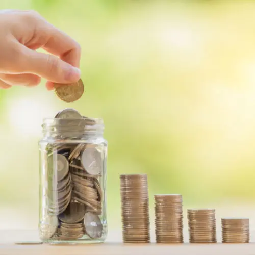 Hand dropping a coin into a savings jar representing retirement annuities and financial growth.