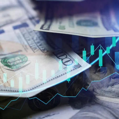 A close-up of one-hundred-dollar bills overlaid with a glowing blue stock market candlestick chart and trend lines.