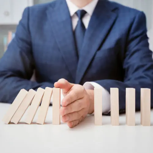 Business professional stopping falling dominoes, representing business protection, risk management, business continuity, loss prevention, and financial security.