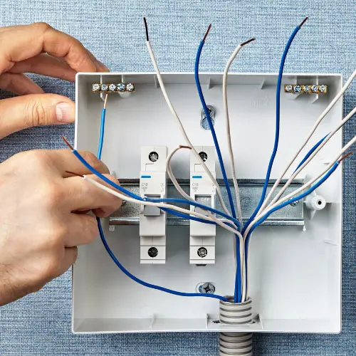 Hands wiring an open electrical breaker panel with blue and white wires, representing equipment breakdown insurance
