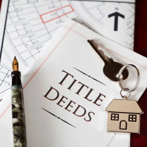 Fountain pen and house-shaped keychain resting on 'Title Deeds' document over a property survey map, representing the ethical title agent
