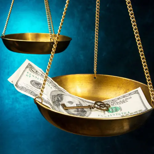 Golden scales of justice weighing cash and a key against blue background, representing ethics and fraud training for insurance adjusters