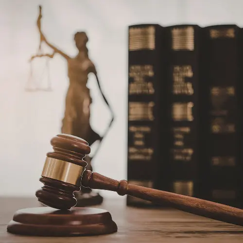 Wooden gavel and law books with a blurred lady justice statue in the background, representing everyday law for insurance agents