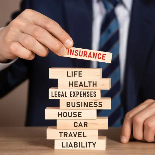 Businessman stacking wooden blocks labeled with insurance types like life, health, business, and liability, representing an insurance industry digest