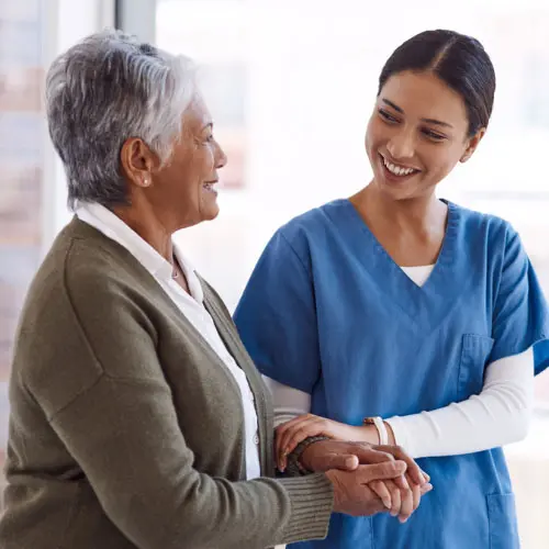 A compassionate caregiver supporting a senior woman in a long-term care setting