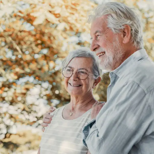 Smiling senior couple standing outdoors among autumn leaves, representing California life insurance policies