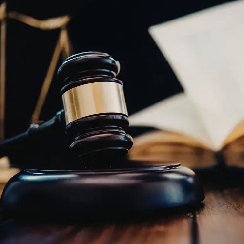 Wooden gavel on its sound block with an open law book and scales of justice blurred in the background, representing public adjuster law