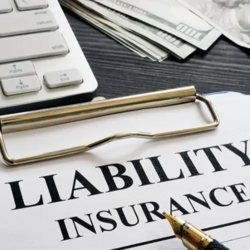 Clipboard with 'Liability Insurance' document, pen, cash, and keyboard on a dark desk, representing understanding liability coverage