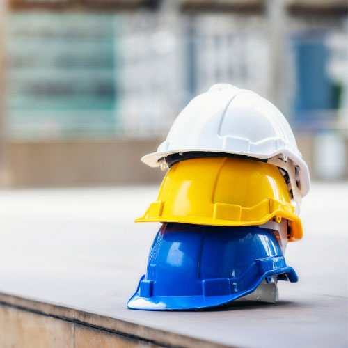Stack of white, yellow, and blue hard hats on a construction site ledge, representing workers' compensation insurance for employees