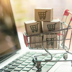 Miniature shopping cart with package boxes on a laptop keyboard representing online product bundles and e-commerce.
